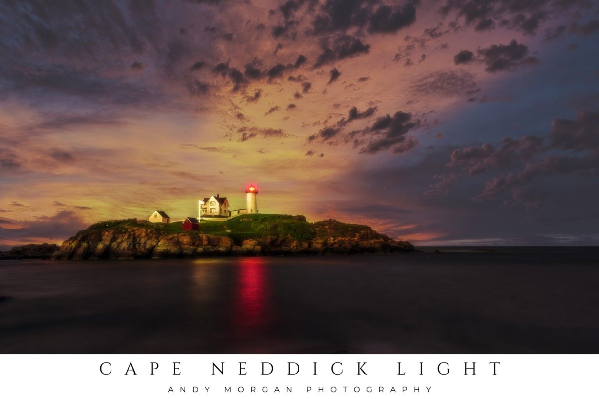 Cape Neddick Nubble Lighthouse on a rocky island illuminated under a dramatic sunset sky with orange and purple clouds, reflected in the dark water below.