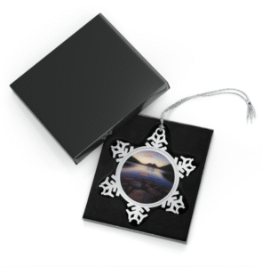 A snowflake-shaped pewter ornament featuring a photograph of Jordan Pond in Acadia National Park at sunset, with mountains and reflections.