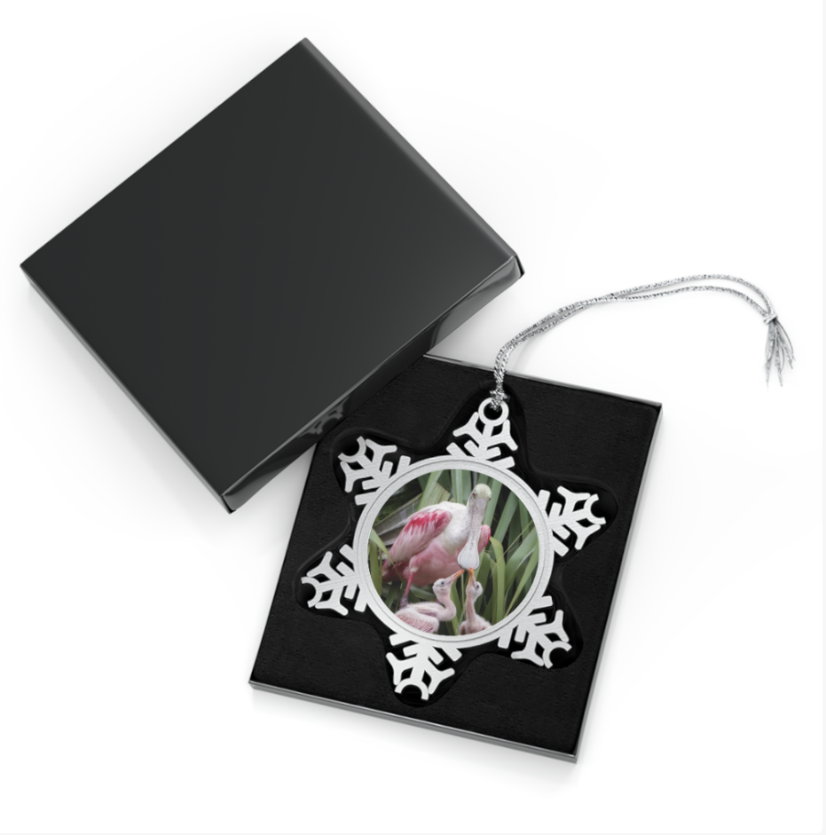 A snowflake-shaped pewter ornament featuring a tender photograph of an adult roseate spoonbill gently interacting with a younger, smaller spoonbill, both with pink plumage.