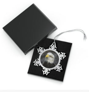 A snowflake-shaped pewter ornament featuring a striking close-up photograph of a bald eagle's head, showing its white head, brown body, and yellow beak.