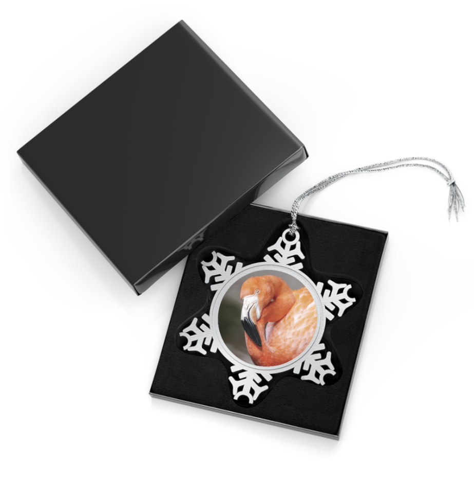 A snowflake-shaped pewter ornament featuring a close-up photograph of a flamingo with its head tucked back, displaying its pink and orange plumage.