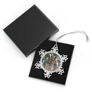 A snowflake-shaped pewter ornament featuring a close-up photograph of a Great Horned Owl perched among branches, with its distinctive ear tufts and intense gaze.
