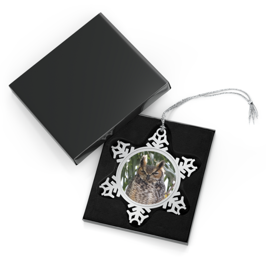 A snowflake-shaped pewter ornament featuring a close-up photograph of a Great Horned Owl perched among branches, with its distinctive ear tufts and intense gaze.