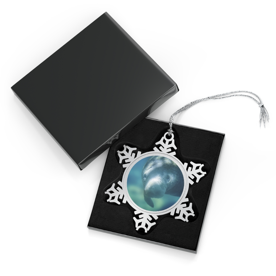 A snowflake-shaped pewter ornament featuring a close-up photograph of a manatee underwater, showing its gentle face and flipper.