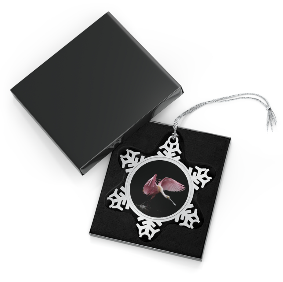A snowflake-shaped pewter ornament featuring a close-up photograph of a roseate spoonbill in flight, surrounded by a silver frame.