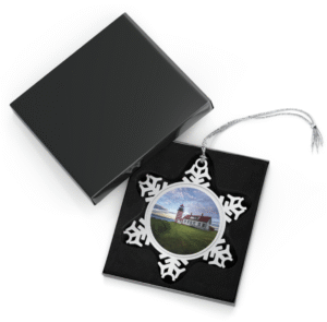 A snowflake-shaped pewter ornament featuring a photograph of the red and white striped West Quoddy Head Lighthouse, with a green lawn in front and a blue sky with clouds.
