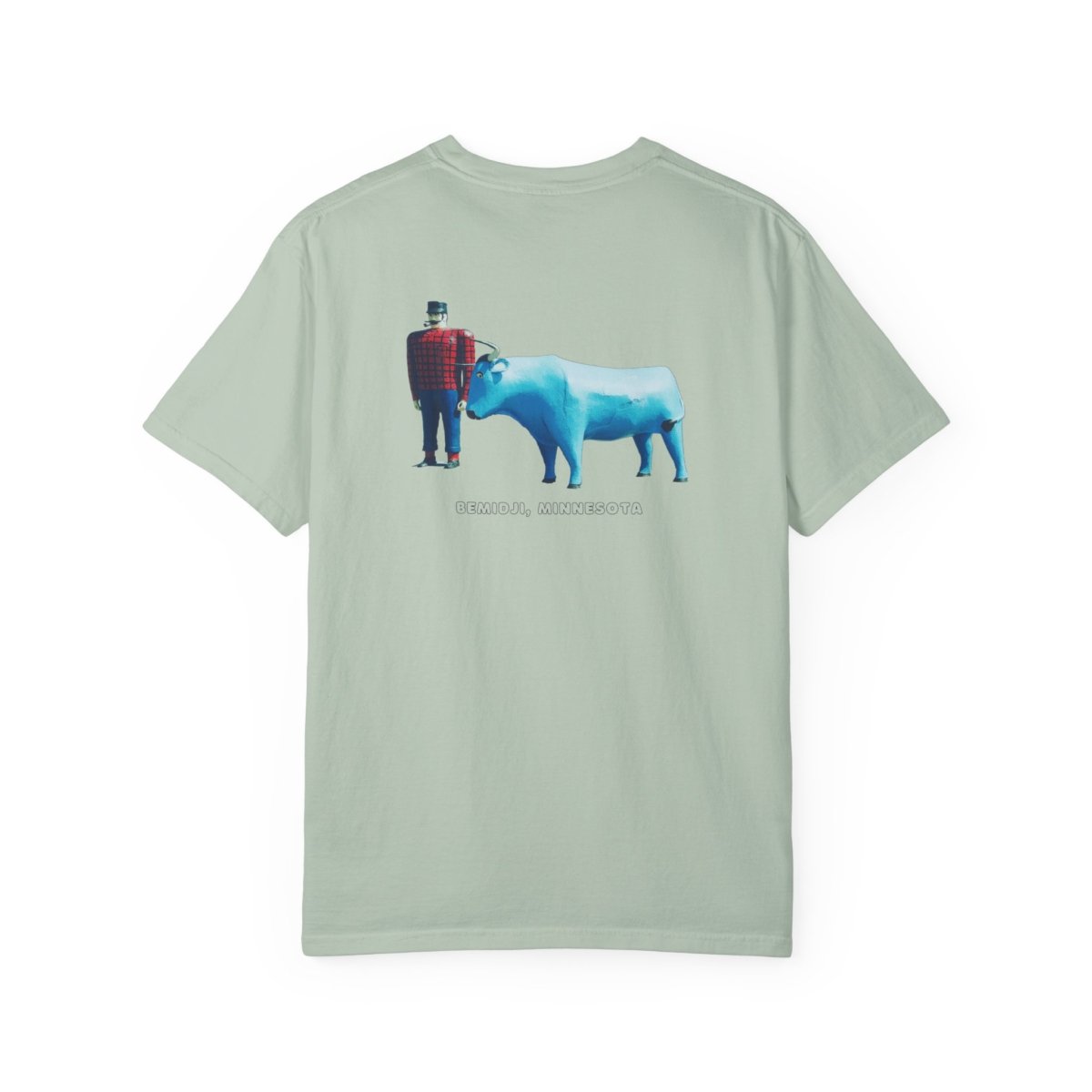 Light green t-shirt featuring a graphic of the Paul Bunyan and Babe the Blue Ox statues in Bemidji, Minnesota. Paul Bunyan is wearing a red and black plaid shirt, and Babe is a large blue ox. The text "BEMIDJI, MINNESOTA" is visible below the statues.