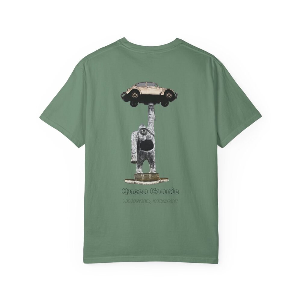 Olive green t-shirt featuring a graphic of the Queen Connie statue. The statue depicts a large white gorilla holding up a beige Volkswagen Beetle car above its head. Text below the graphic reads "Queen Connie" and "LEICESTER, VERMONT."