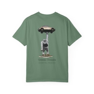 Olive green t-shirt featuring a graphic of the Queen Connie statue. The statue depicts a large white gorilla holding up a beige Volkswagen Beetle car above its head. Text below the graphic reads "Queen Connie" and "LEICESTER, VERMONT."
