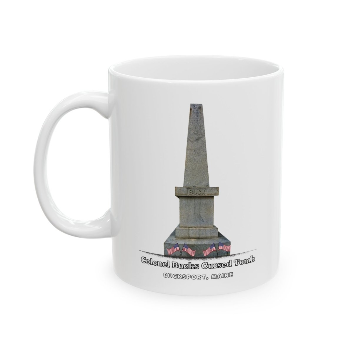 A white ceramic coffee mug with a graphic of a tall, grey stone obelisk with a dark stain near the base, and text that reads "Colonel Bucks Cursed Tomb BUCKSPORT, MAINE."
