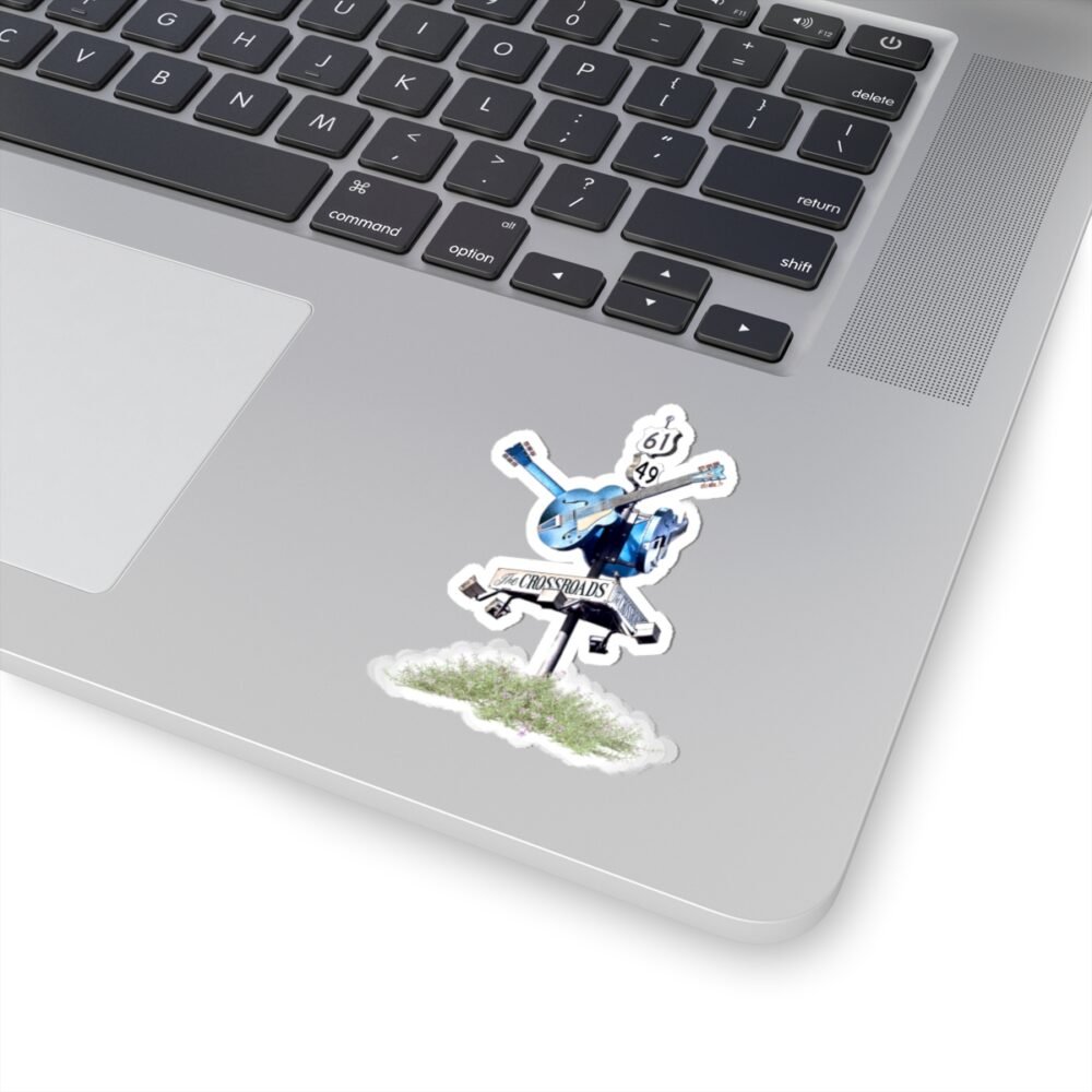 Laptop with a sticker of a blues crossroads sign with a blue guitar and "THE CROSSROADS" text.