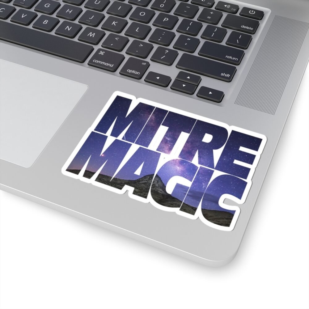 Laptop with a "MITRE MAGIC" sticker featuring a starry night sky over mountains.