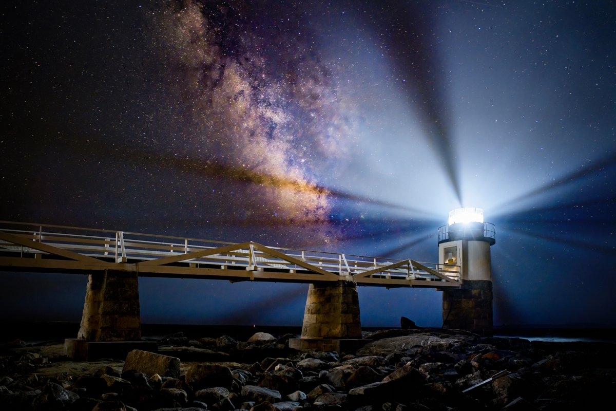 Marshall Point Lighthouse in Port Clyde, Maine, under a breathtaking view of the Milky Way stretching across the starry night sky.