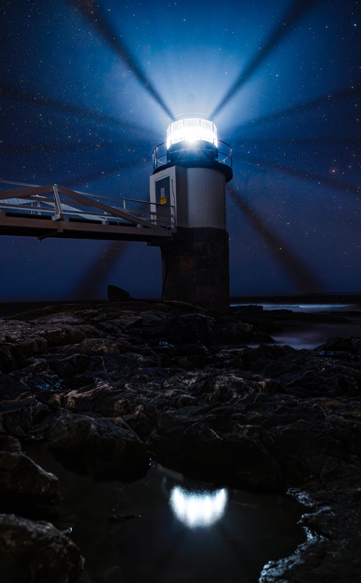 Marshall Point Lighthouse in Port Clyde, Maine. The picture shows a long, beautiful walkway and the light tower with beams of light shining out.