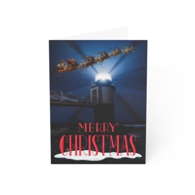 Christmas notecard with a bright spotlight beam from Marshall Point Lighthouse illuminating Santa's sleigh and reindeer in the dark blue night sky. Bold red text reads "Merry Christmas."